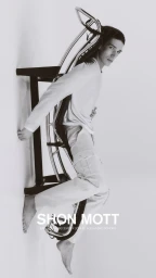 Model leaning against a metal furniture frame wearing white clothing against a seamless white background.