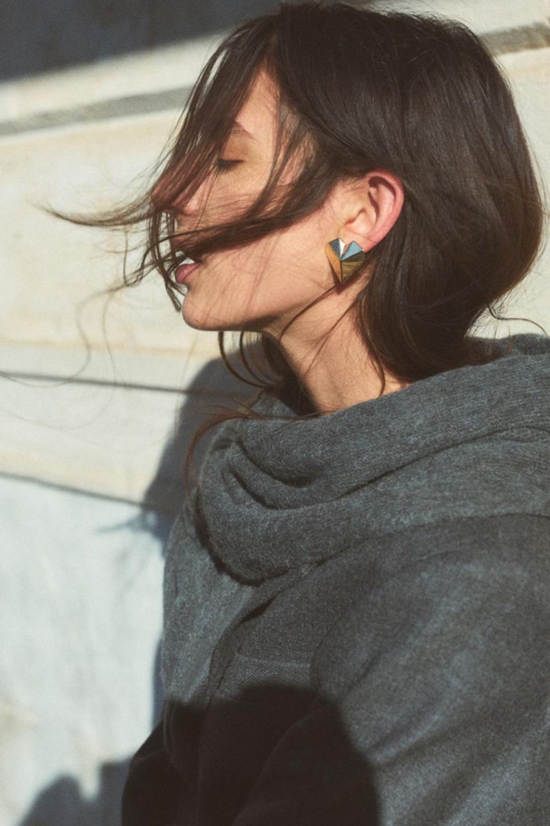 Profile portrait of a woman wearing a dark grey hoodie and geometric earrings with hair blowing across her face
