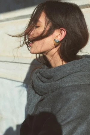 Profile portrait of a woman wearing a dark grey hoodie and geometric earrings with hair blowing across her face