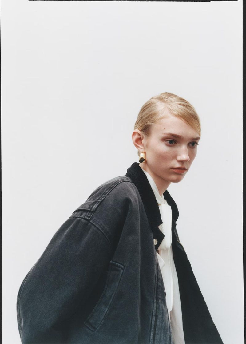 Portrait of a blonde woman in a denim jacket and blouse, posing against a white backdrop, showcasing fashion and editorial style.