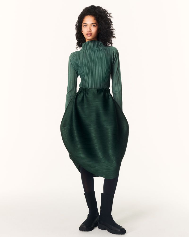 Model wearing a pleated green top and structured green skirt against a white studio background for Issey Miyake.