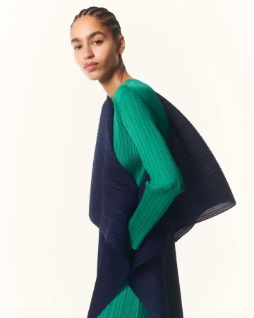 Model wearing a vibrant green pleated top layered under a dark navy pleated garment against a seamless white background.