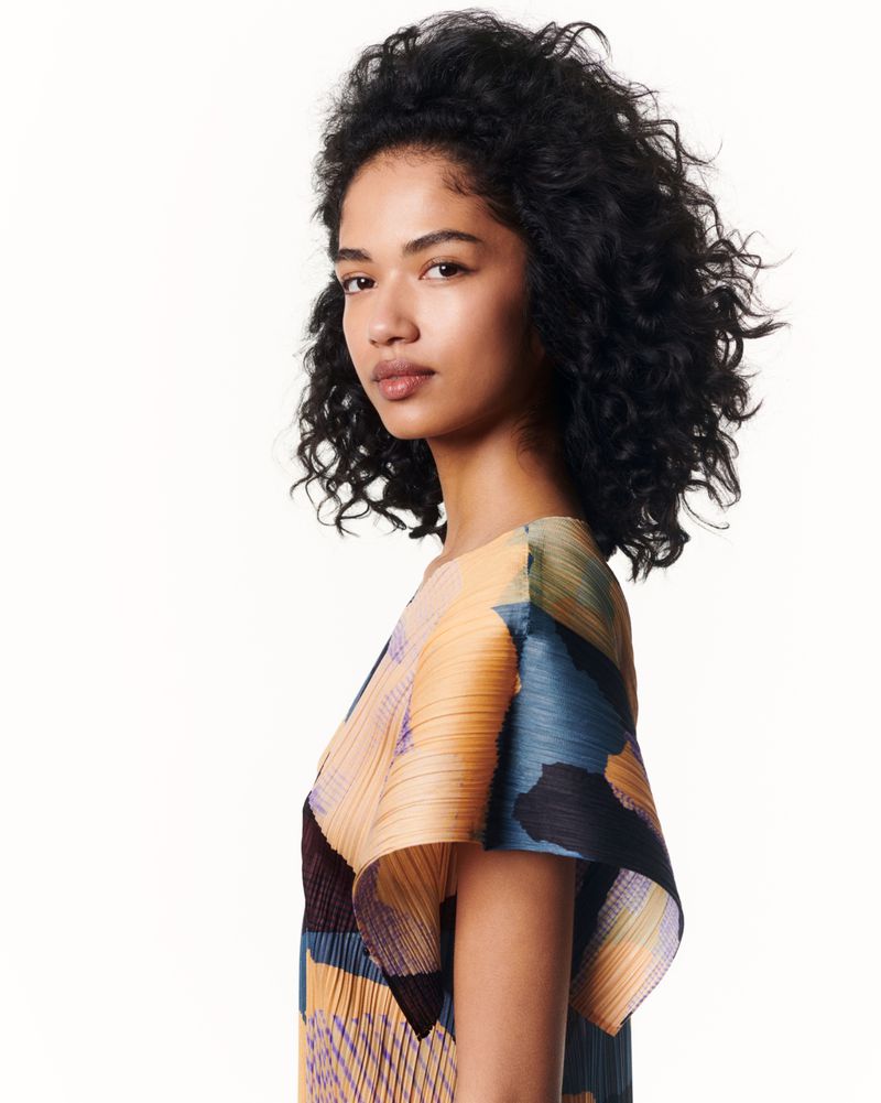 Portrait of a female model wearing a patterned pleated top against a plain white background for Issey Miyake.