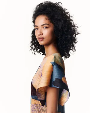 Portrait of a female model wearing a patterned pleated top against a plain white background for Issey Miyake.
