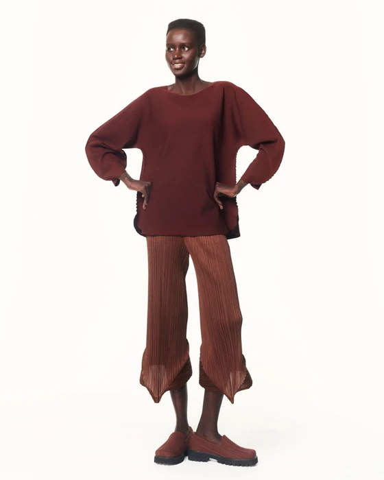 Model standing against a white seamless background wearing a pleated burgundy top and matching trousers