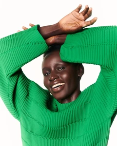 Model wearing a vibrant green pleated top with arms raised against a bright white background