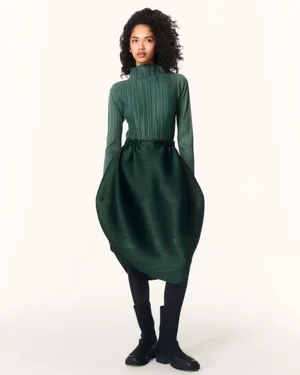 Model wearing a pleated green top and structured green skirt against a white studio background for Issey Miyake.
