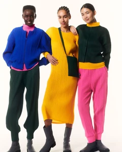Three female models posing in brightly colored pleated garments against a seamless white background for Issey Miyake Pleats Please F/W 24