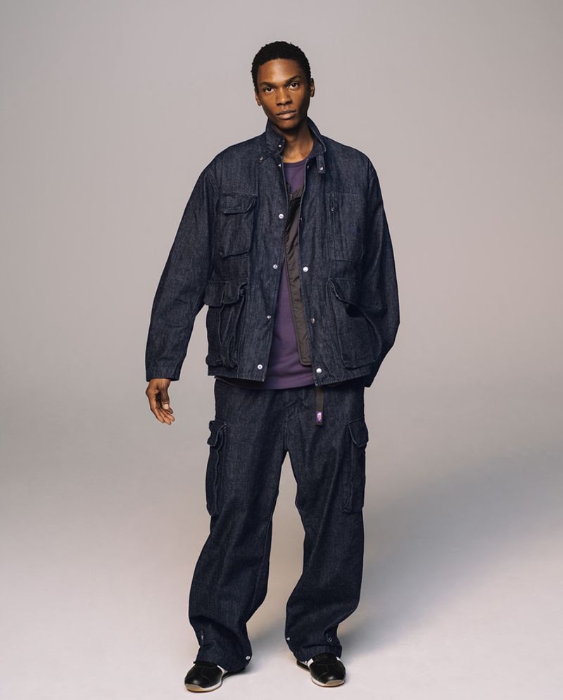 Full-length shot of an adult Black male in a photo studio. He is wearing a dark blue denim jacket and matching cargo pants.