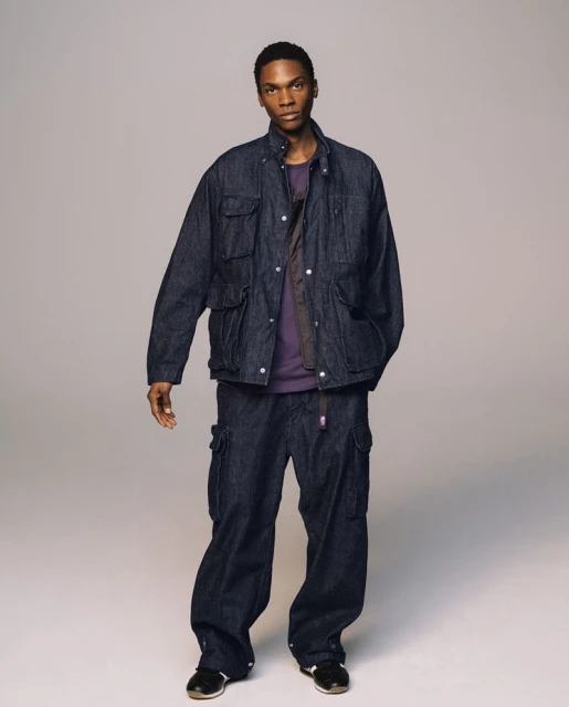 Full-length shot of an adult Black male in a photo studio. He is wearing a dark blue denim jacket and matching cargo pants.