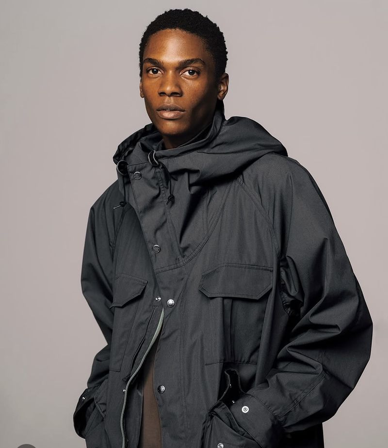 Model wearing a dark grey hooded jacket against a seamless neutral studio background
