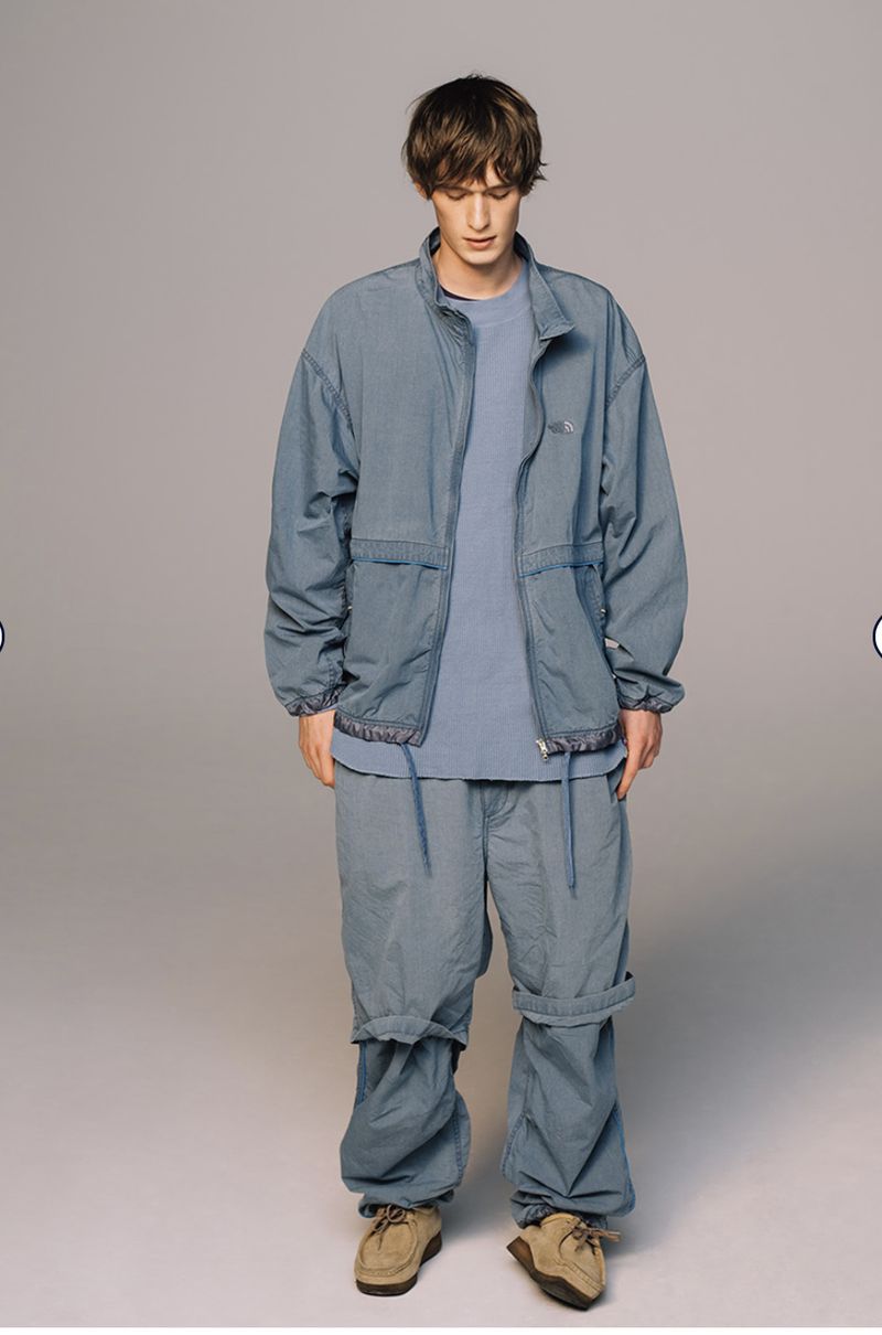 Full-length shot of a male model in a blue-grey matching jacket and pants, complemented by light brown shoes against a neutral backdrop.