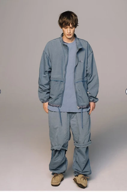 Full-length shot of a male model in a blue-grey matching jacket and pants, complemented by light brown shoes against a neutral backdrop.
