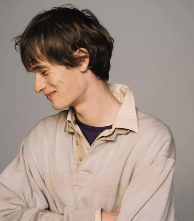 Portrait of young male model smiling with eyes closed wearing beige polo shirt against a grey seamless background