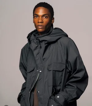 Model wearing a dark grey hooded jacket against a seamless neutral studio background