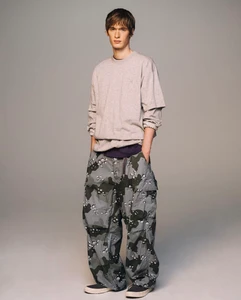 Model wearing a grey crewneck sweatshirt and patterned camouflage cargo pants against a plain studio background.