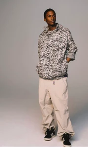 Model standing against a grey backdrop wearing a patterned anorak jacket and light trousers