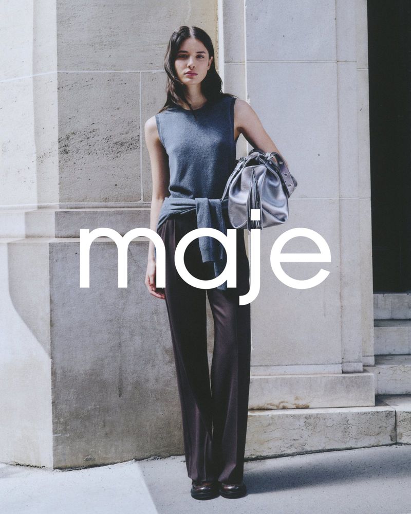 Fashionable adult woman wearing a sleeveless top, draped sweater, and flared pants, posing with a silver purse in an outdoor setting.