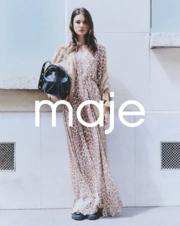 Fashion shot of a woman wearing an animal print maxi dress and a tan cardigan, holding a black bucket bag against a white wall.