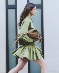 Model in green outfit walking past a building exterior holding a brown fringed handbag for Maje FW24 Lookbook