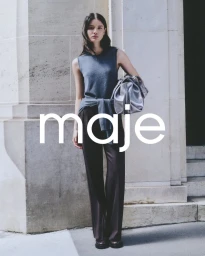 Model standing outdoors wearing a grey sleeveless top and dark trousers holding a silver handbag in front of a stone building.