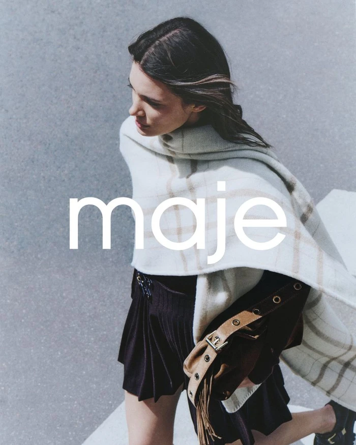 Model in plaid scarf and dark skirt walking outdoors with a fringe handbag for Maje FW24 Lookbook