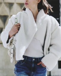 Model wearing a white faux fur jacket and blue denim jeans carrying a white handbag