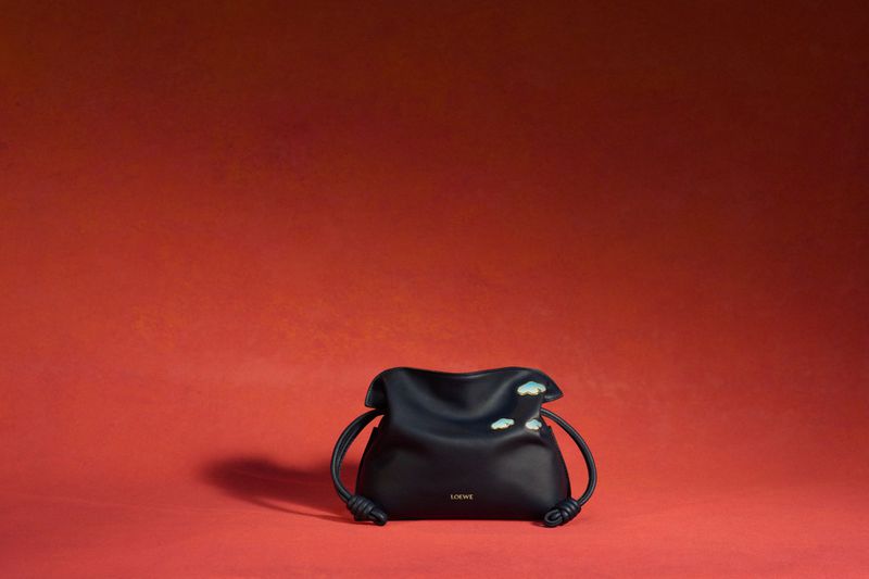 Loewe pouch bag in black leather with cloud details against a vivid red backdrop, conveying modern luxury and minimalist fashion.