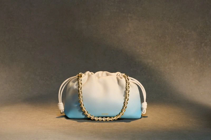 Elegant handbag with an ombre blue and white color scheme, gold chain, and gathered fabric, presented against a neutral backdrop.
