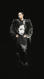 A model wearing an oversized structured black jacket and graphic t-shirt against a plain black background.
