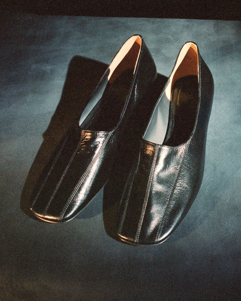 Pair of shiny black leather heeled shoes on a textured blue background, lit to emphasize the smooth material and elegant design.