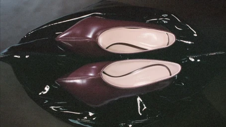 Burgundy pointed-toe leather shoes resting on a glossy black textured surface