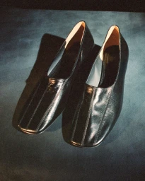 A pair of sleek black leather shoes with square toes resting on a dark mottled surface.