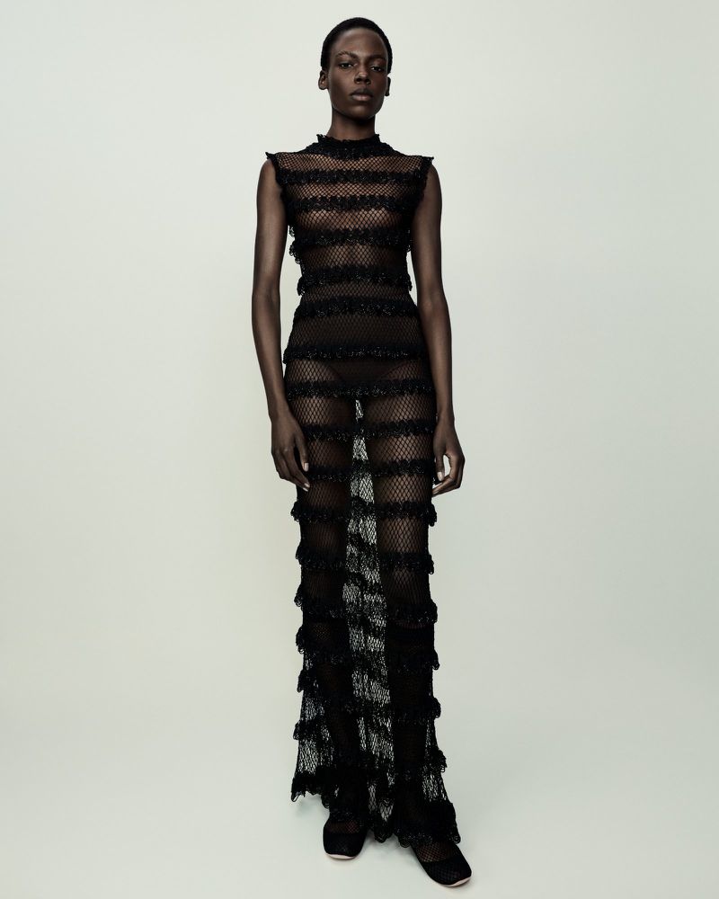 Model standing in a sheer black striped maxi dress against a plain neutral background