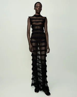 Model standing in a sheer black striped maxi dress against a plain neutral background