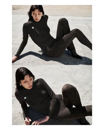 Model Jay Pak wearing a fitted dark patterned long-sleeve top and leggings, posed outdoors on a concrete ground.