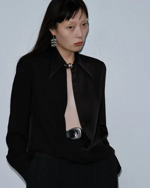 Model wearing a black shirt and earrings against a plain grey backdrop for Beaufille Resort 25