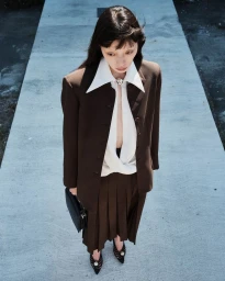 Model wearing brown jacket and white collared shirt standing on concrete path for Beaufille Resort 25