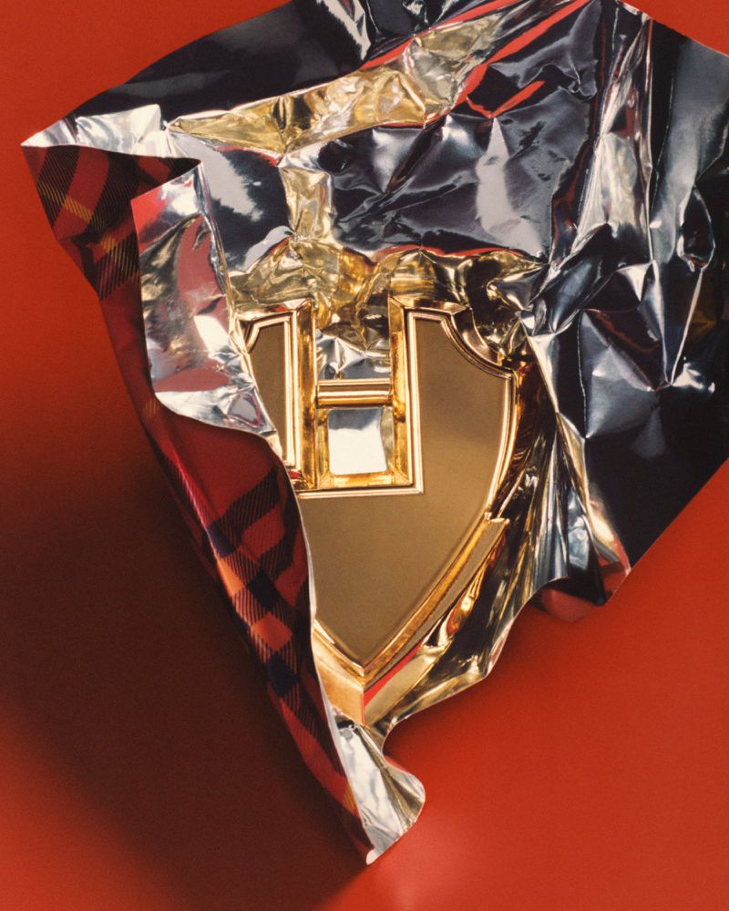 Gold emblem wrapped in silver foil and plaid cloth against a red background creates a luxurious and eye-catching still life photograph.