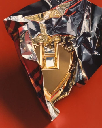 Gold emblem wrapped in silver foil and plaid cloth against a red background creates a luxurious and eye-catching still life photograph.