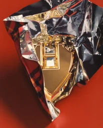 Close-up of a metallic gold monogram clasp wrapped in silver foil and red plaid paper against a solid red background