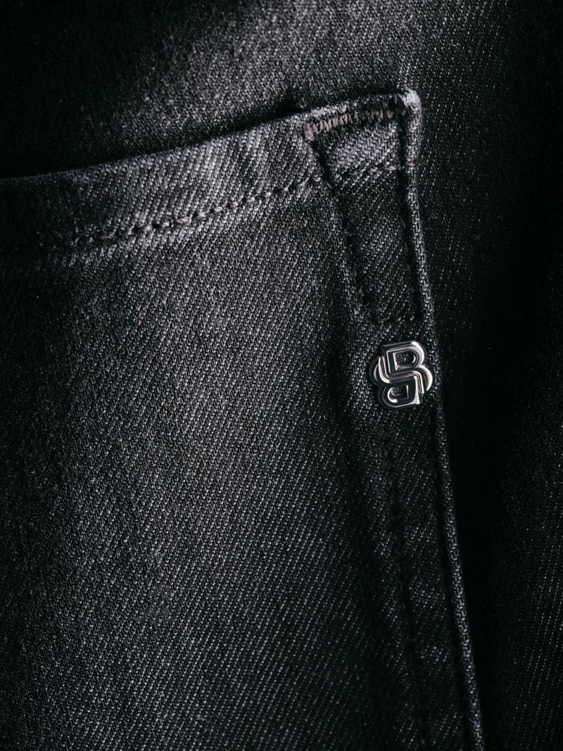 Close-up of black denim fabric with a pocket and a metallic logo button, showcasing texture and detail.