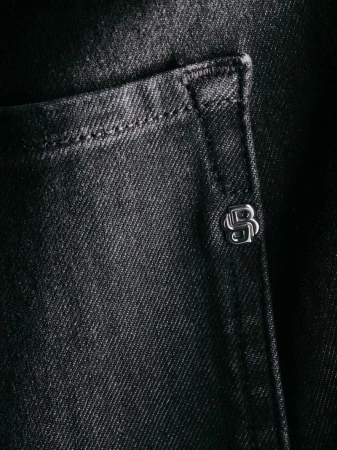 Close-up of black denim fabric with a pocket and a metallic logo button, showcasing texture and detail.