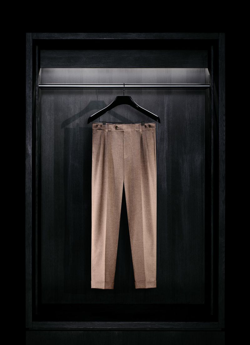 Studio shot of dress pants on a hanger in a black wood frame. Minimalist fashion photography showcases the garment's fabric and cut.