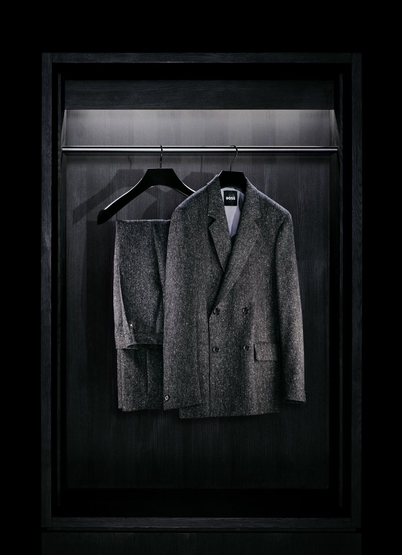 Gray herringbone suit hangs in a dark wooden closet with a silver rod and minimalist lighting, offering a sleek and modern wardrobe image.
