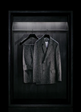 Gray herringbone suit hangs in a dark wooden closet with a silver rod and minimalist lighting, offering a sleek and modern wardrobe image.