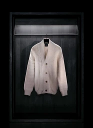 Beige knitted cardigan hanging on a black hanger inside a dark wooden display cabinet by BOSS
