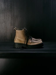 Tan leather lace-up boot with black rubber lug soles on a dark wooden shelf