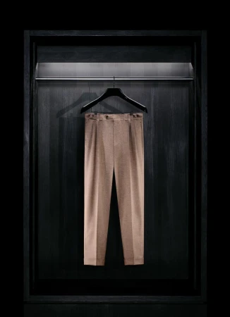 Tailored beige trousers hanging on a black hanger inside a dark wooden illuminated wardrobe alcove