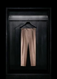 Tailored beige trousers hanging on a black hanger inside a dark wooden illuminated wardrobe alcove